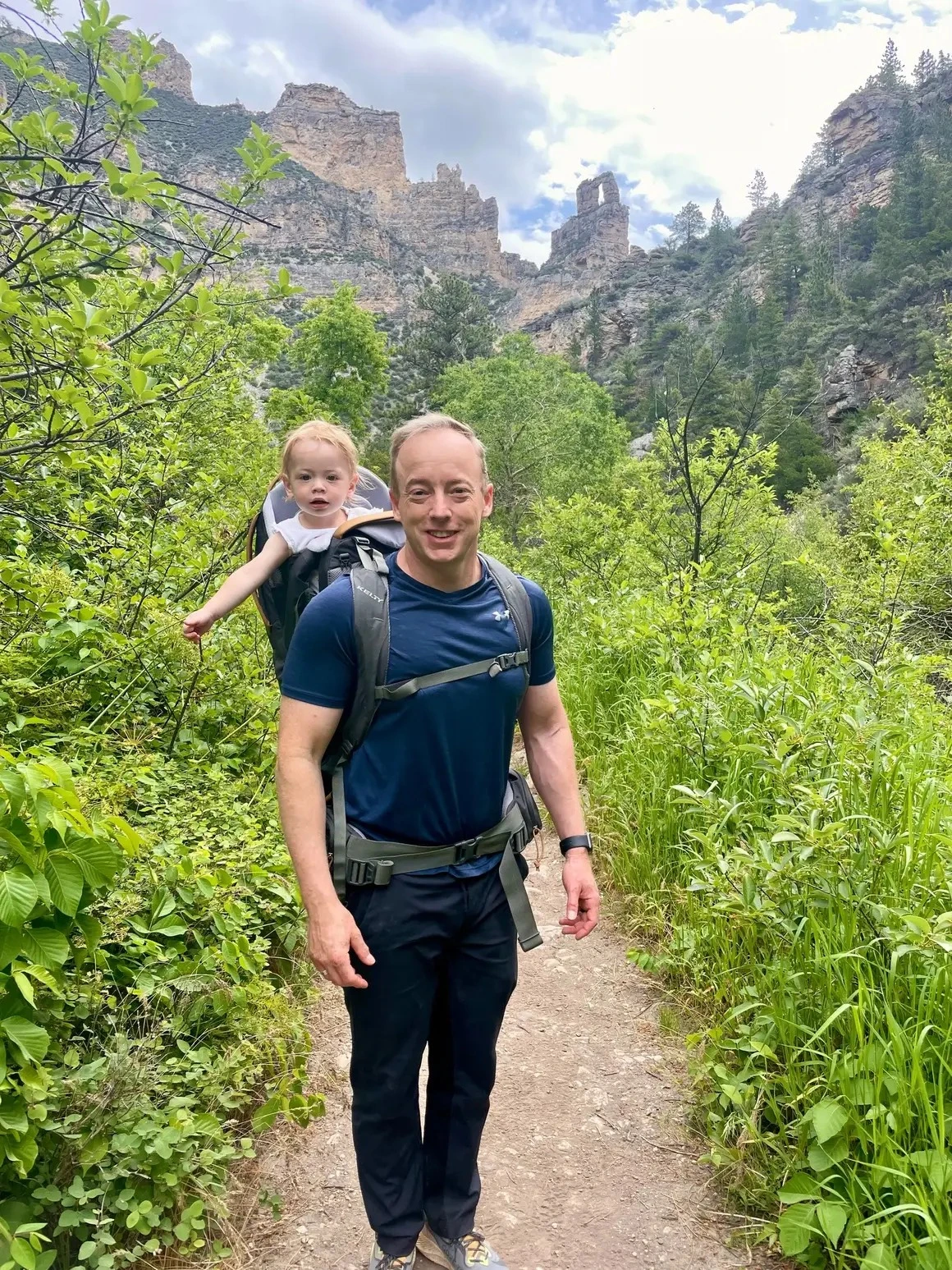 Kelly Johnson hiking through the mountains while carrying his daughter